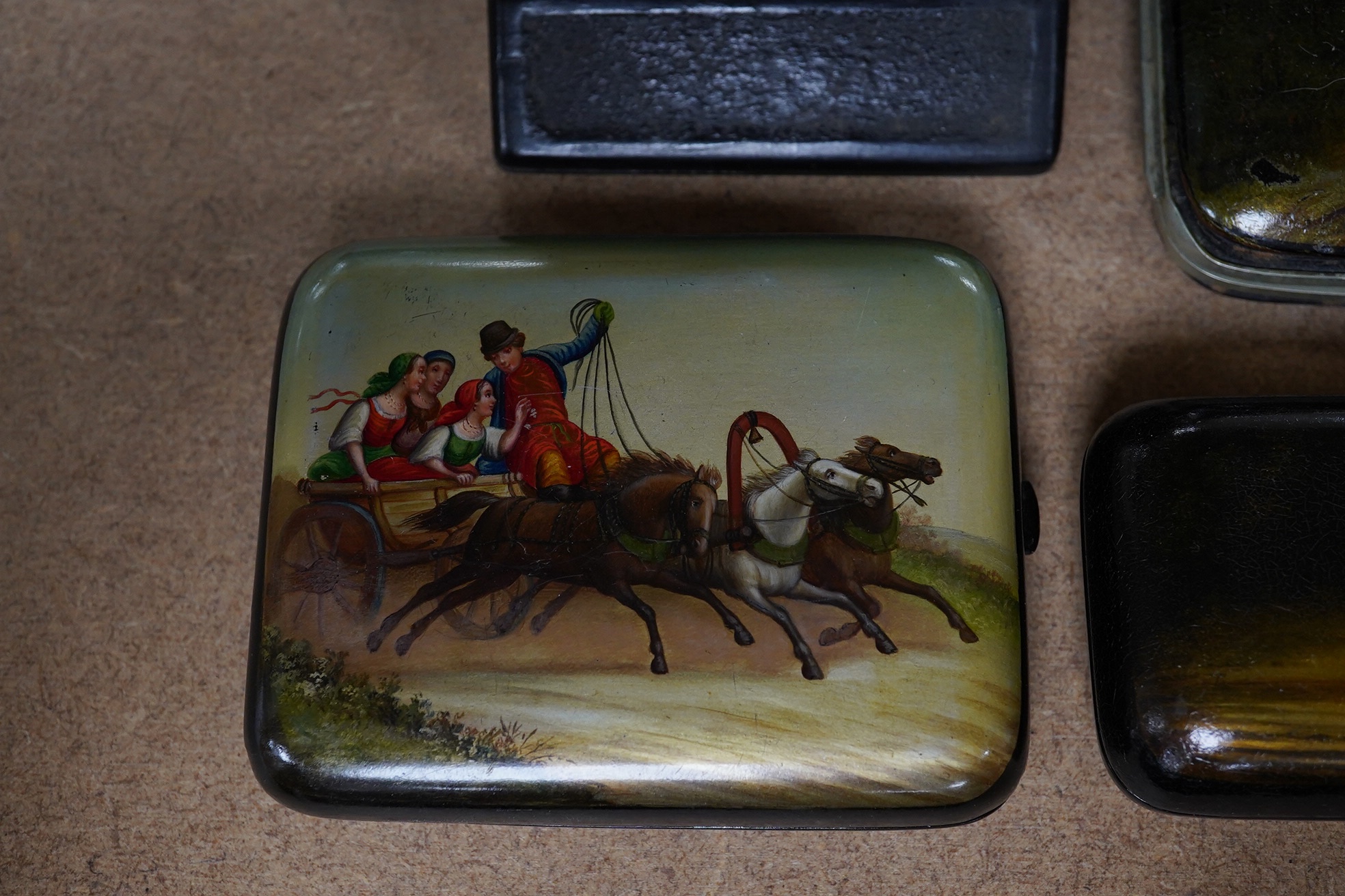 Three Russian lacquer cigarette cases, late 19th/early 20th century, one decorated with a troika scene and a match strike, 11cm wide. Condition - good